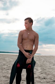 一位年轻男性冲浪者在爱沙尼亚的海滩上摆姿势，背景是晴朗的天空和宁静的大海