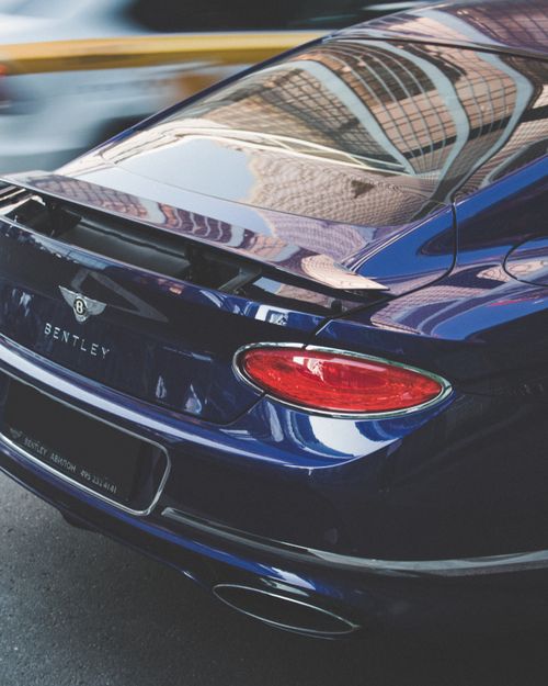 Free Close-up of a luxury blue Bentley sports car reflecting city architecture, showcasing elegance and speed. Stock Photo