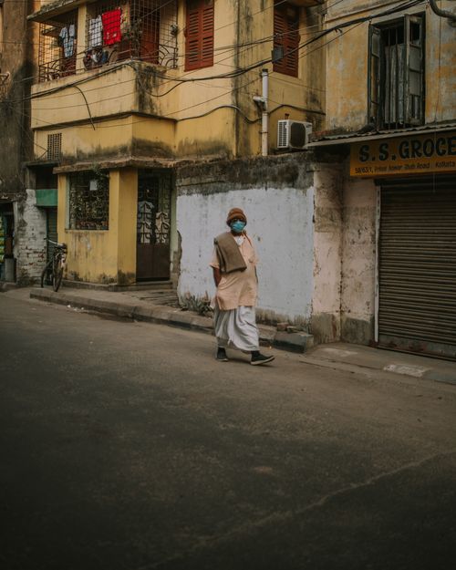 Free Man in face mask walking past old buildings on a quiet urban street corner. Stock Photo