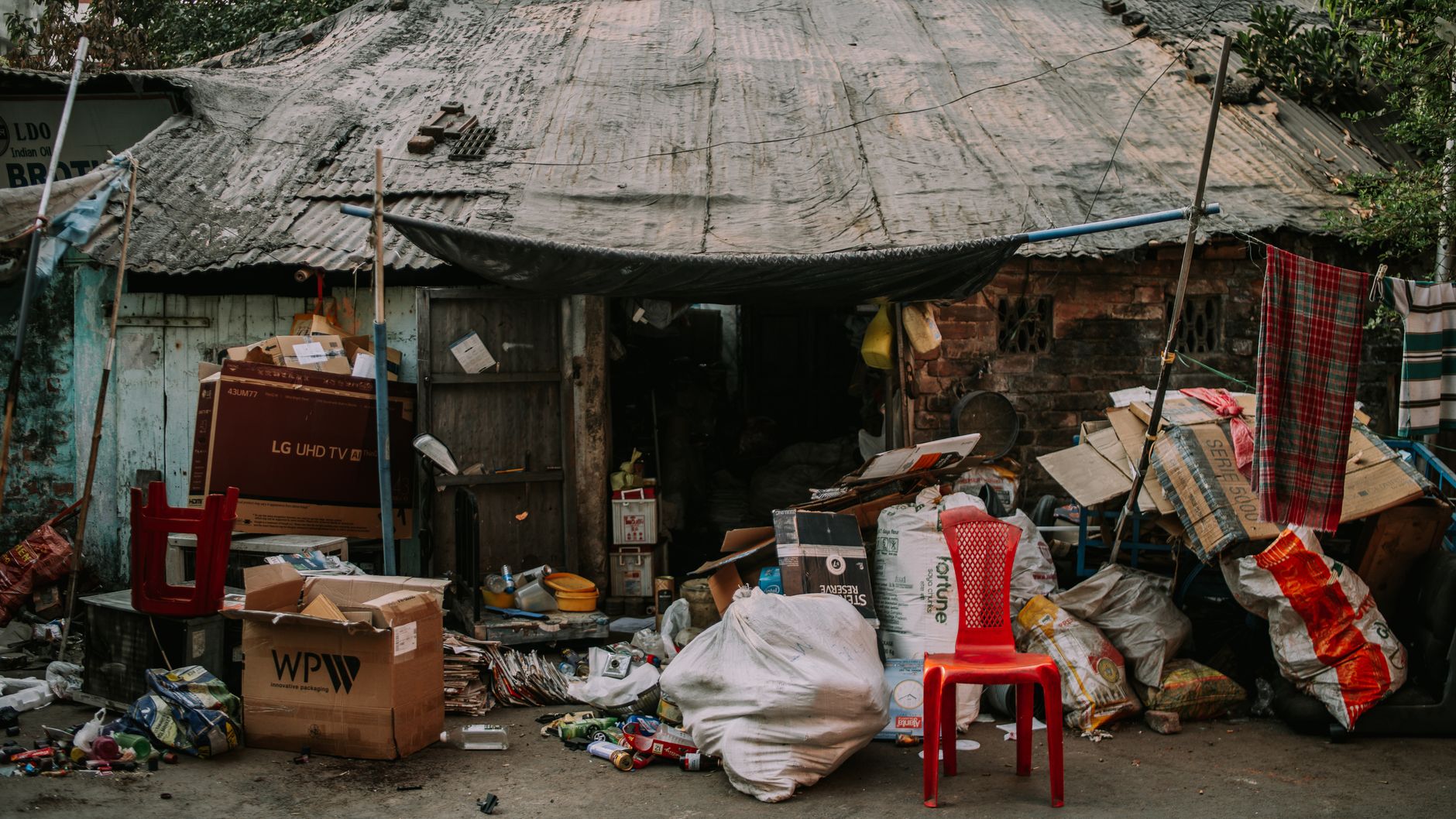 Rustic hut in a rural village with a cluttered entrance and a red plastic chair in front.