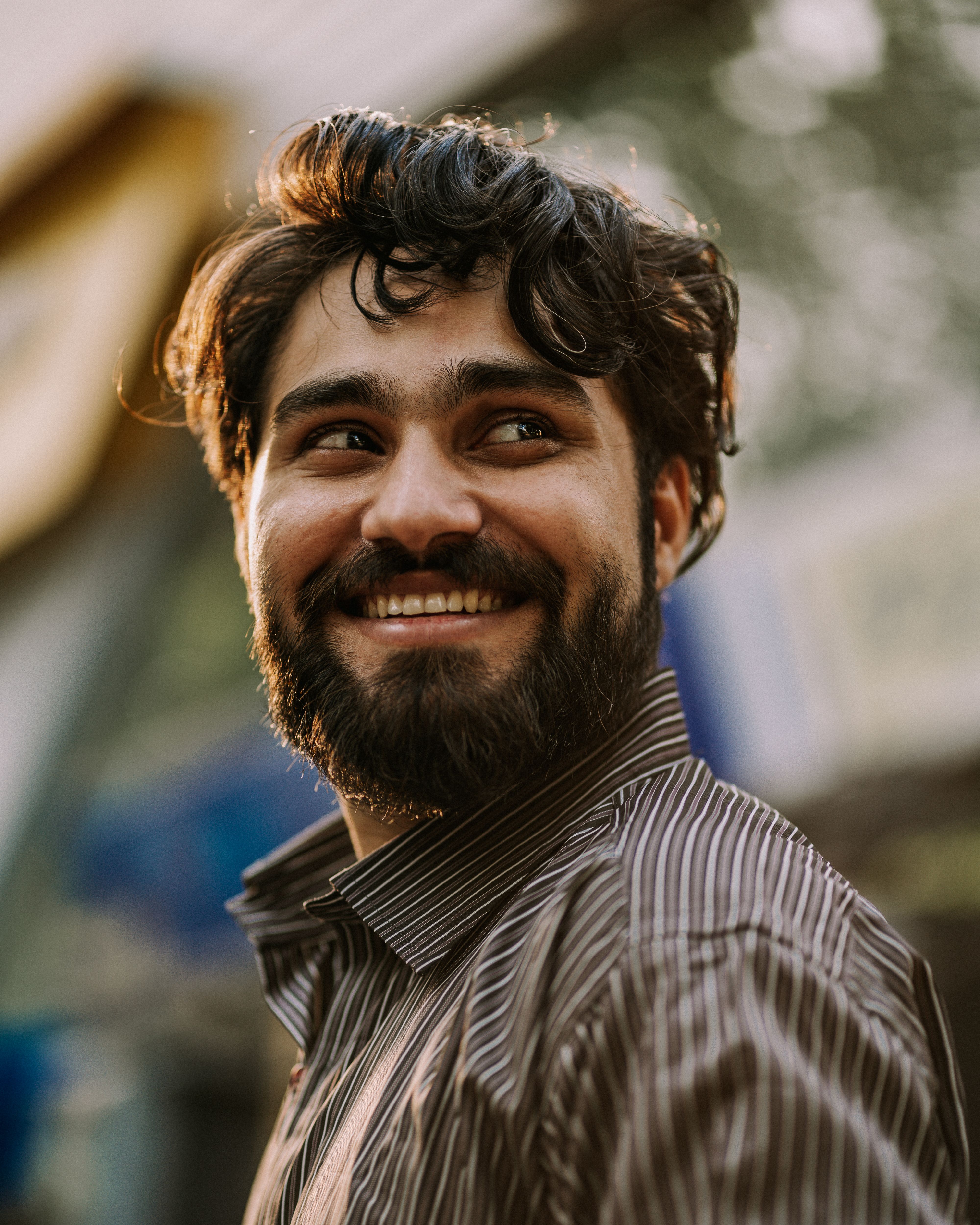 Close-up portrait of a smiling bearded man outdoors, conveying warmth and positivity.