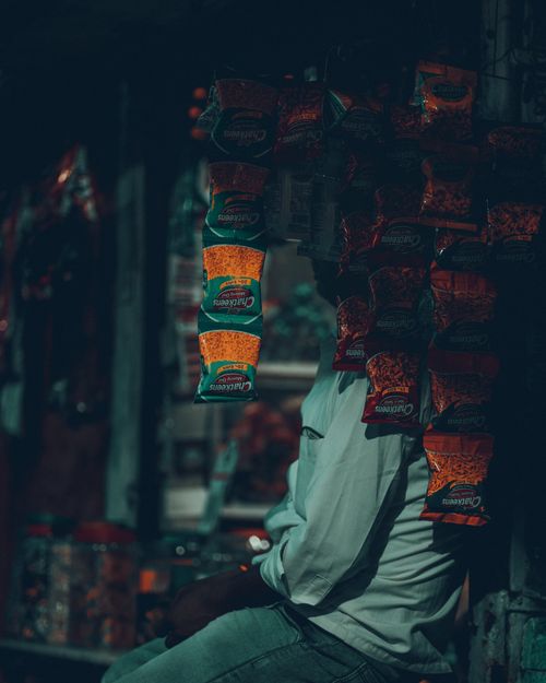 Free Moody street scene featuring a vendor with hanging snack packages in unknown location. Stock Photo