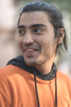 Close-up of a young man in an orange hoodie smiling, showcasing a natural candid expression. - Fotografer Sidoarjo