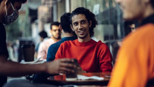 Free Men enjoying a lively conversation at an outdoor café. Warm and inviting atmosphere. Stock Photo