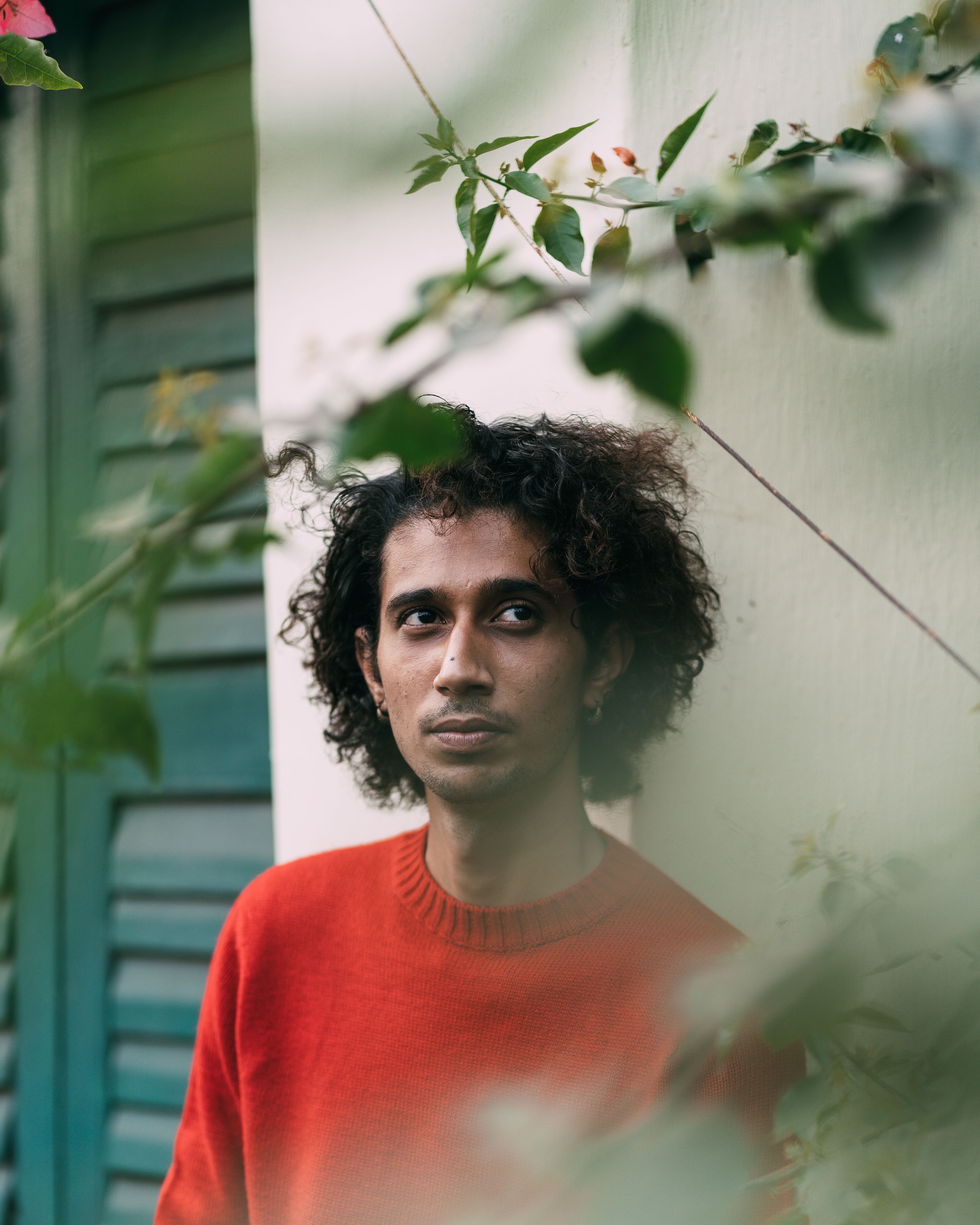 Young man in red sweater amidst greenery, creating a serene and introspective mood.