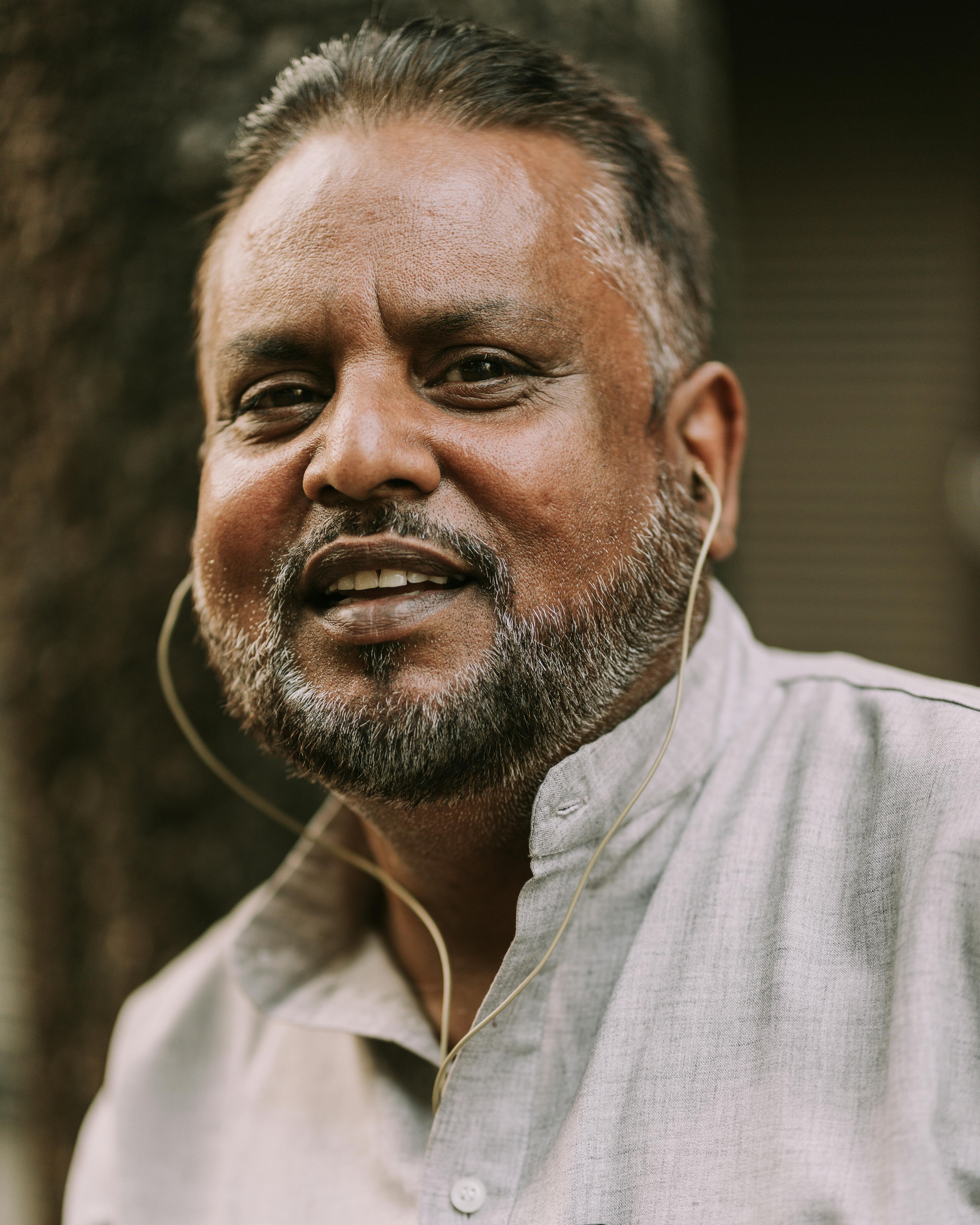 Middle-aged man with a beard, smiling wearing earphones outdoors. Warm and friendly portrait.