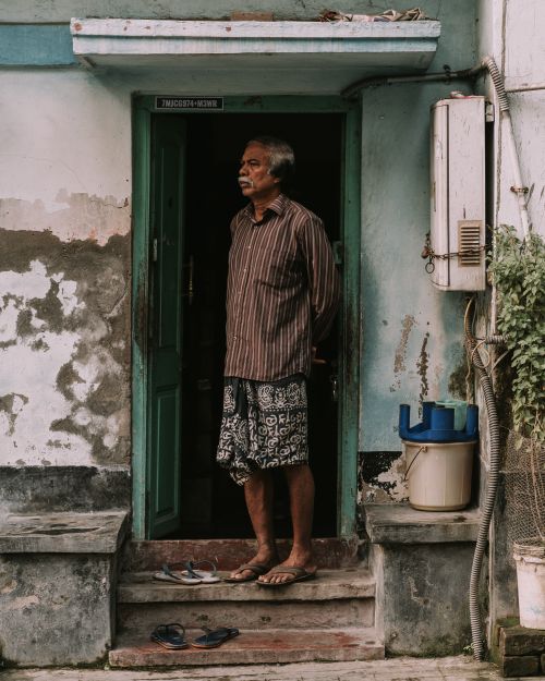 Free An elderly man stands in the doorway of a rustic building, embodying wisdom and solitude. Stock Photo