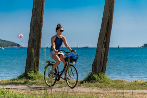 Woman in Blue Tank Top and Blue Shorts Riding on Bicycle Near Body of Water during