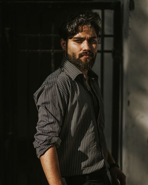 Free Portrait of a man with a beard in a striped shirt, standing outdoors in natural light. Stock Photo