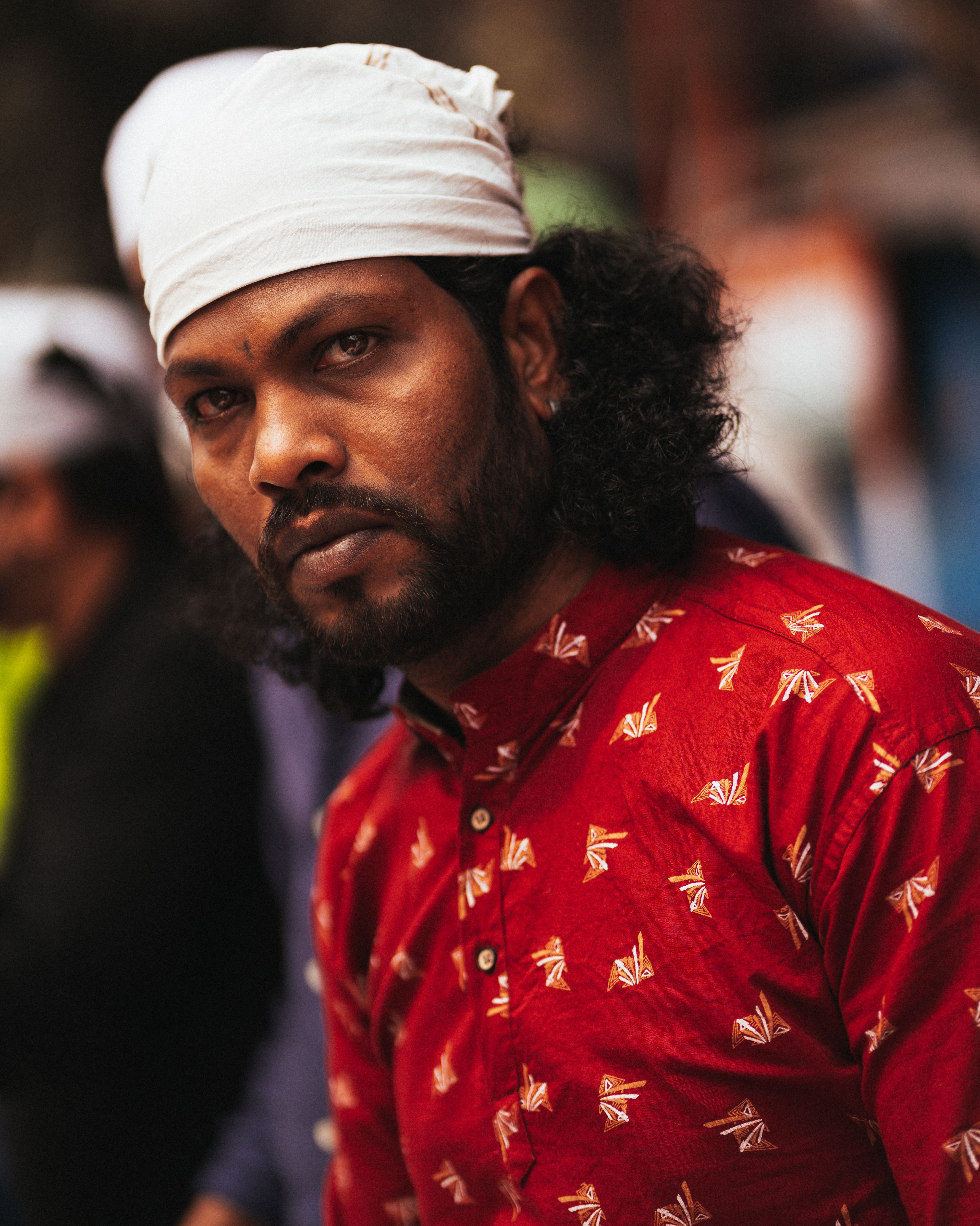 A striking portrait of a man in red traditional attire with a focused expression, headscarf detail.