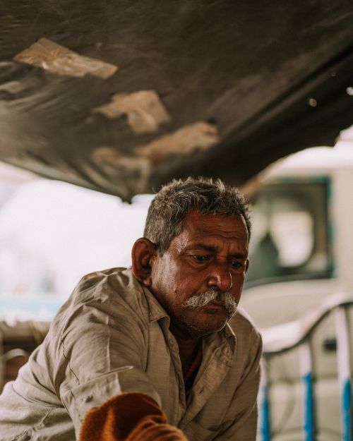 Free An elderly man with a mustache looks contemplative under a tarp, wearing casual clothing. Stock Photo