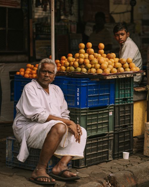 Free An outdoor market scene featuring two men selling fresh fruits from a sidewalk stand. Stock Photo