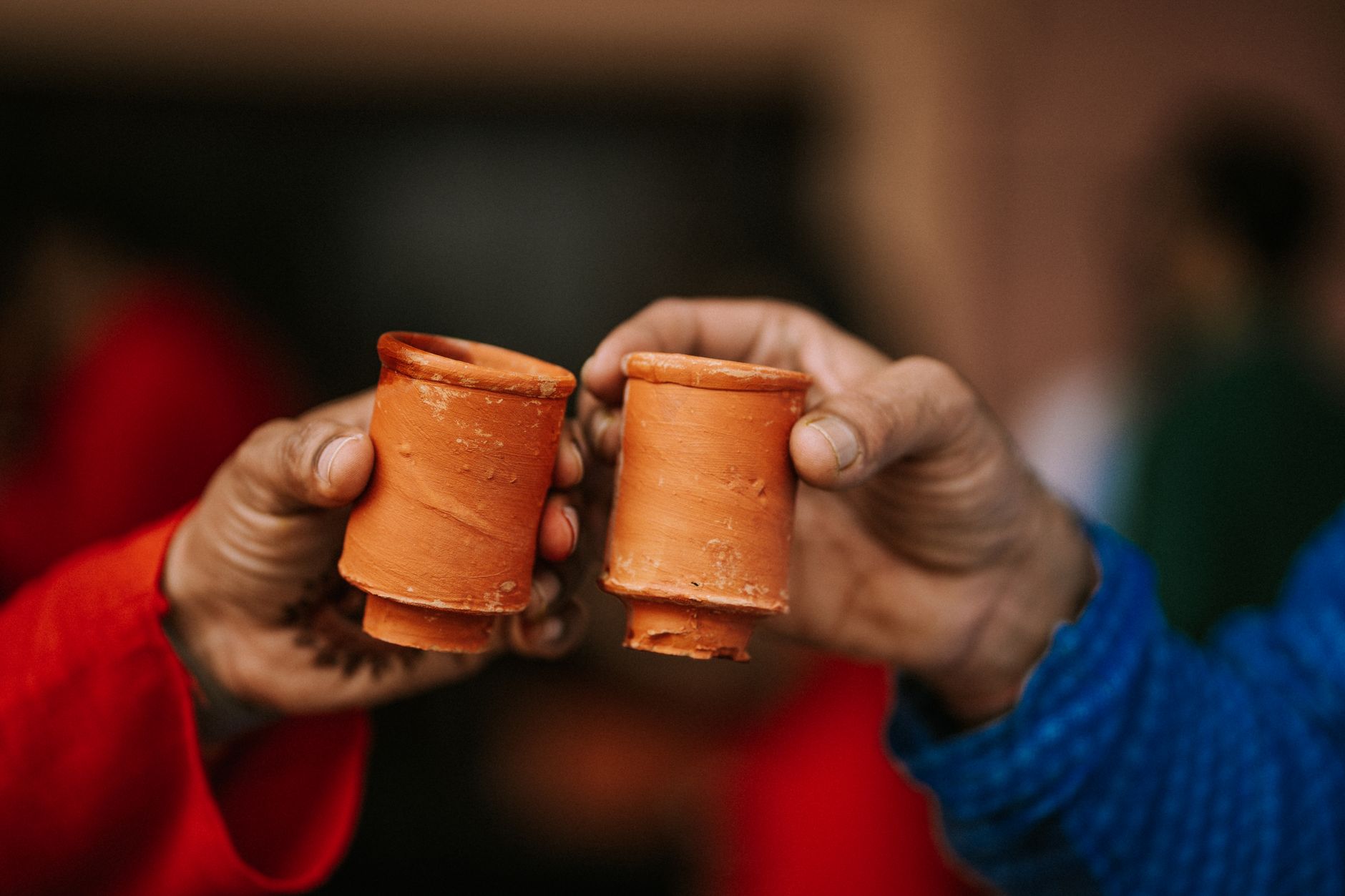 Two people celebrating with handmade clay cups, toasting in a warm, festive setting.