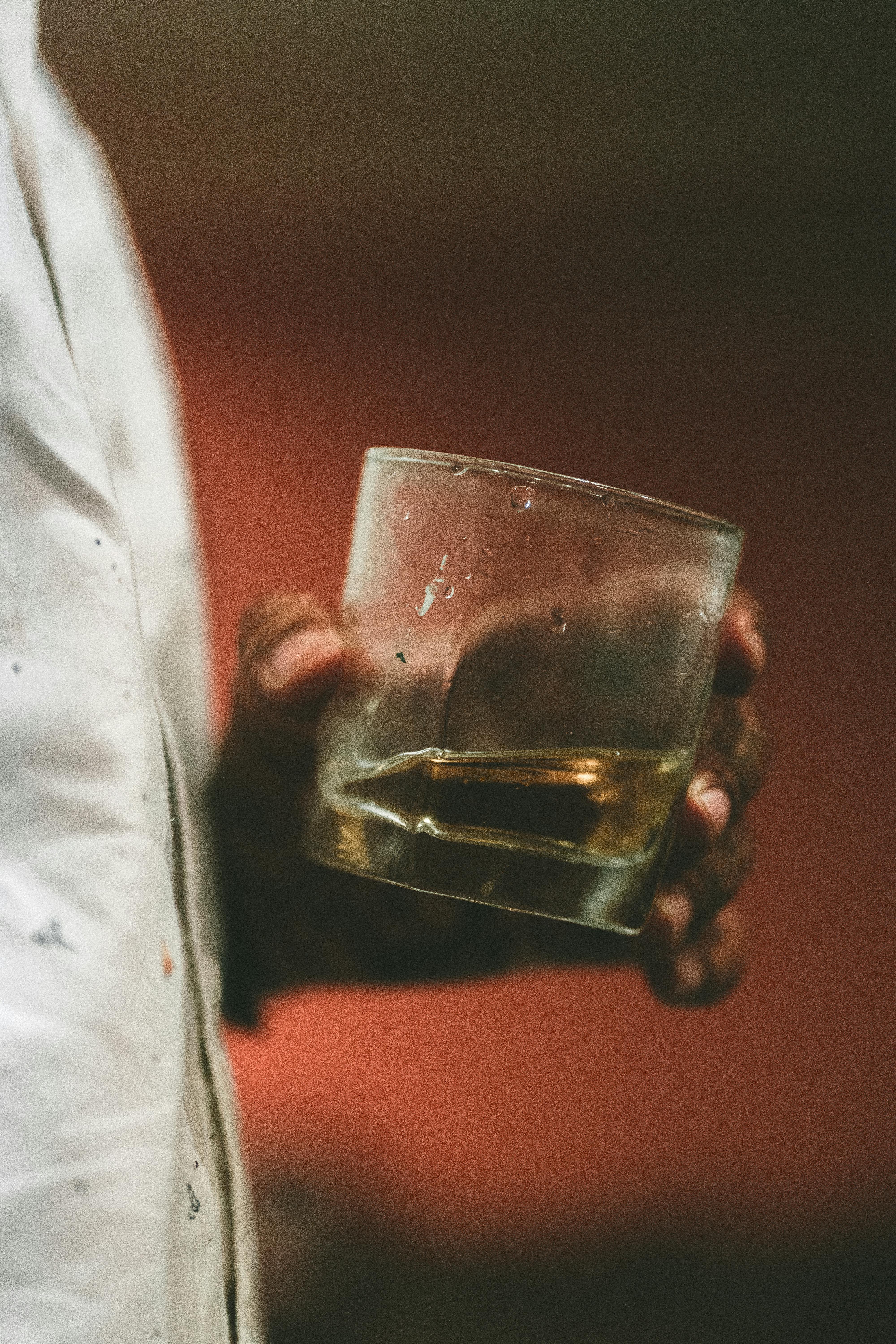 A hand holding a glass with a beverage in a close-up shot with warm lighting.