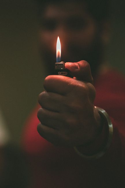 A detailed view of a hand holding a lighter with a flame in focus, emphasizing warmth and light.