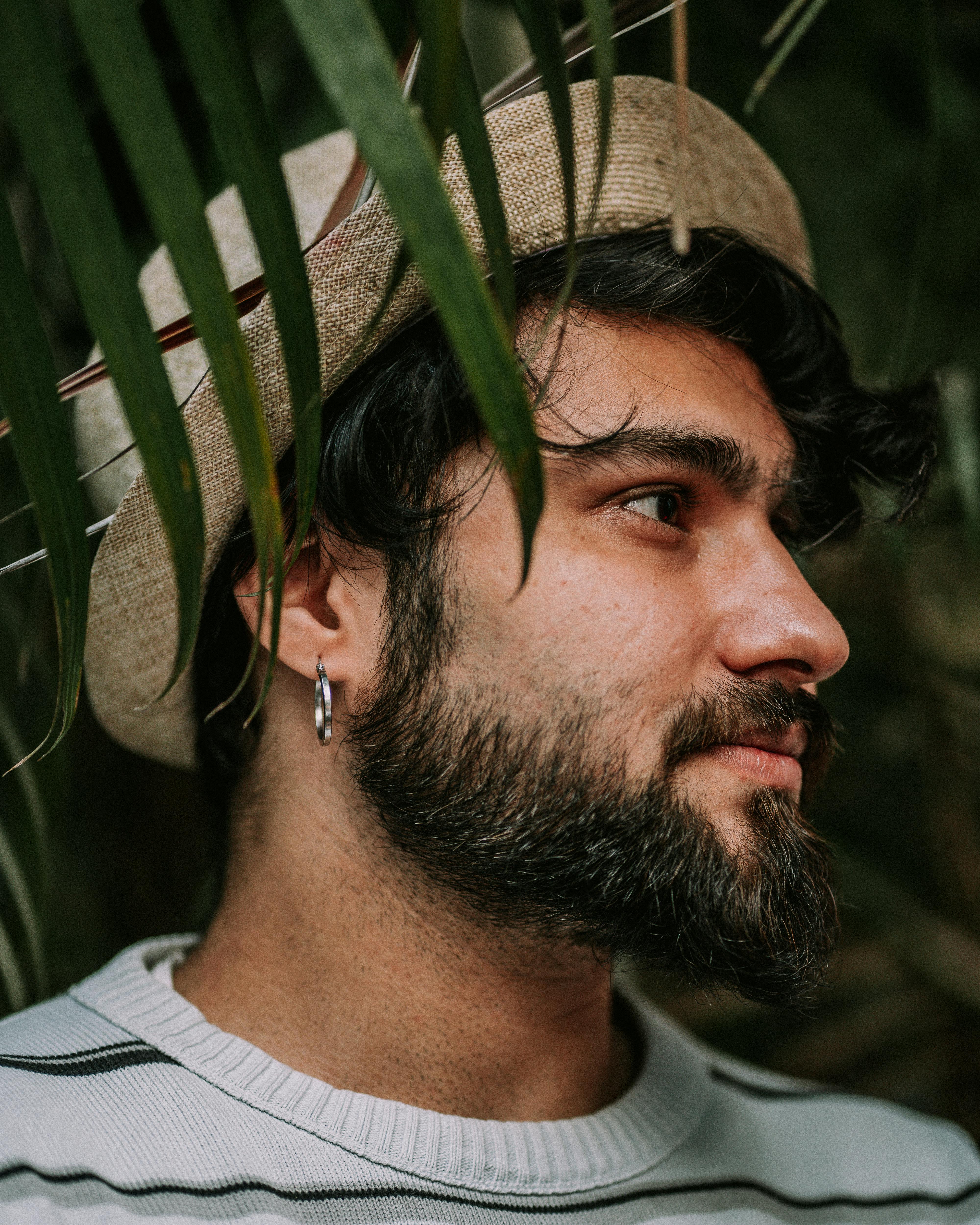Side profile portrait of a young man with a beard in a straw hat surrounded by foliage.