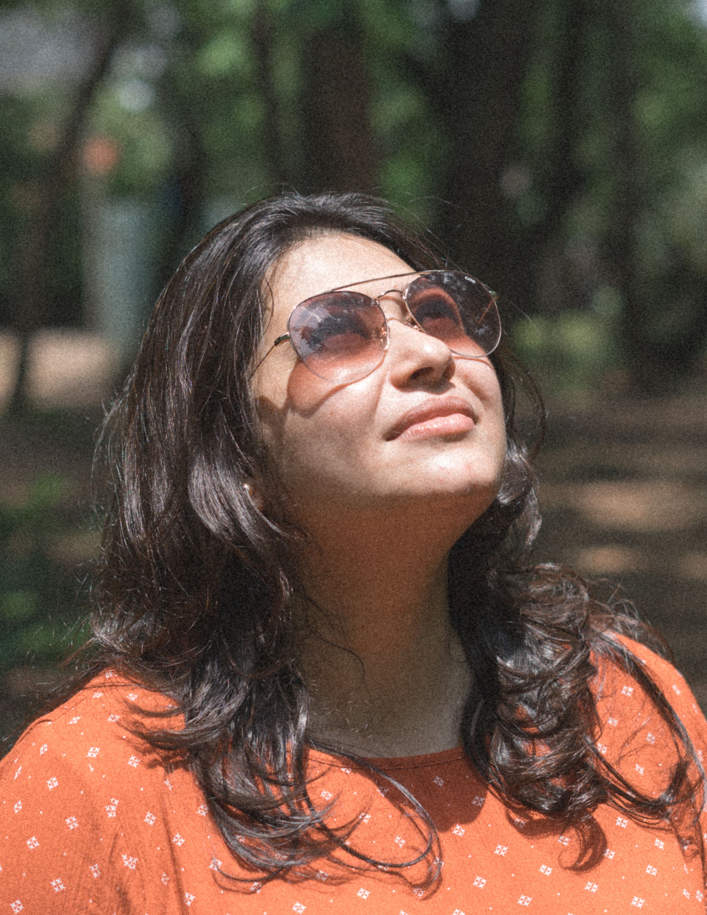 Close-up portrait of a woman with sunglasses looking up in a sunlit forest.