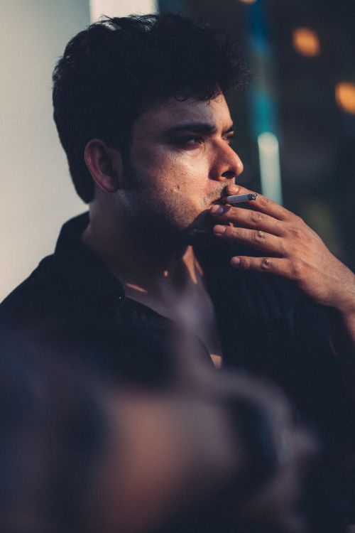 Free Close-up of a man in a black shirt smoking a cigarette with dramatic lighting. Stock Photo