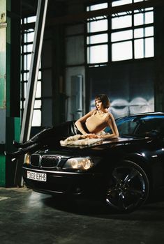 Elegant woman posing on a luxury car indoors, showcasing style and sophistication.