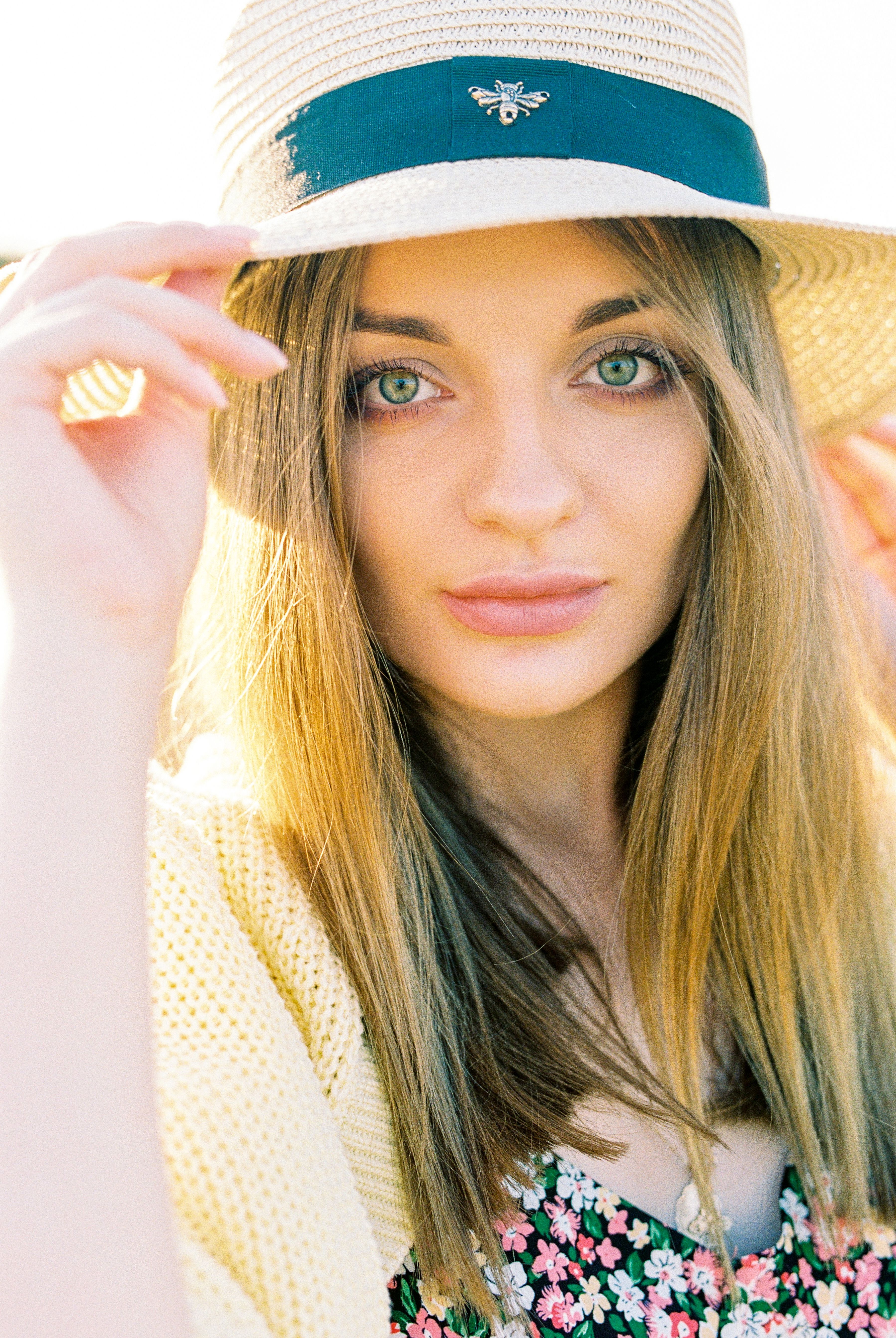 Close-up portrait of a woman wearing a sun hat with green eyes and flowing hair.