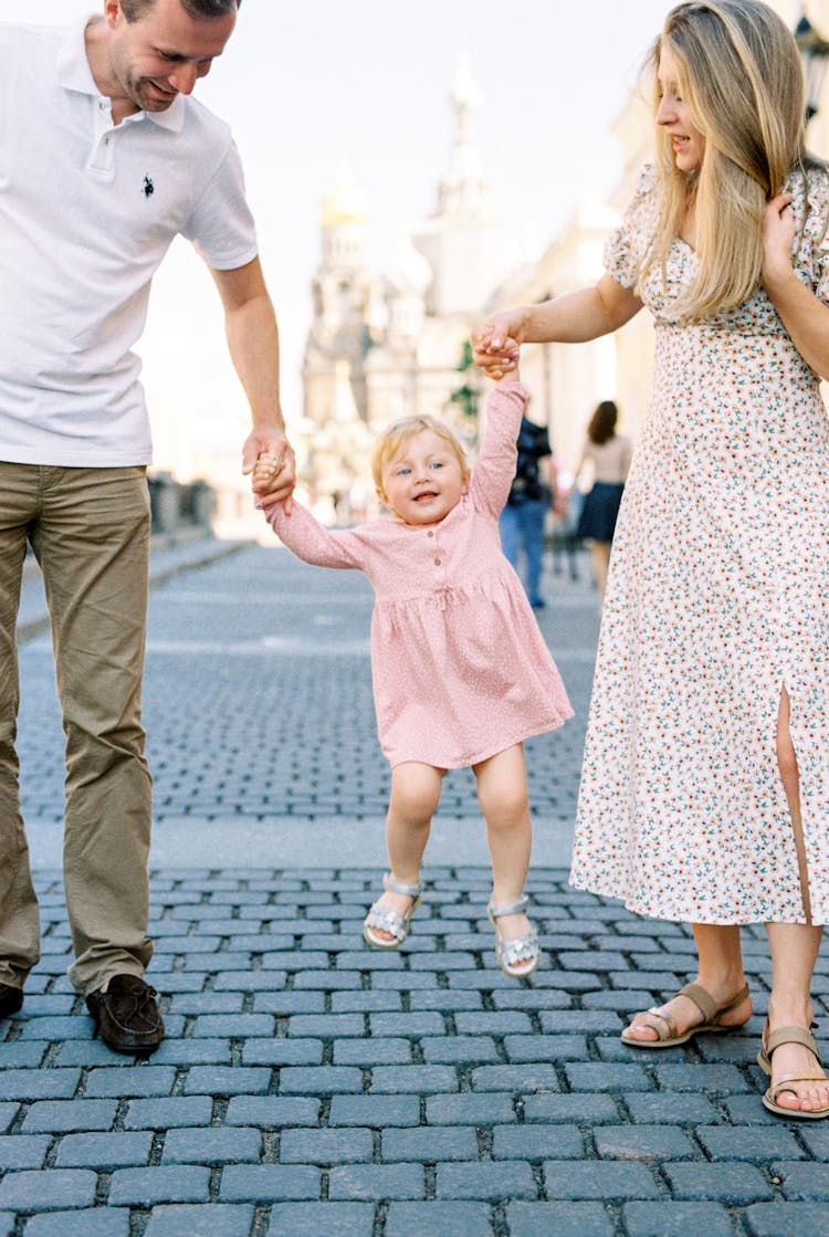 Mom And Dad Swinging Their Cheerful Baby Daughter 