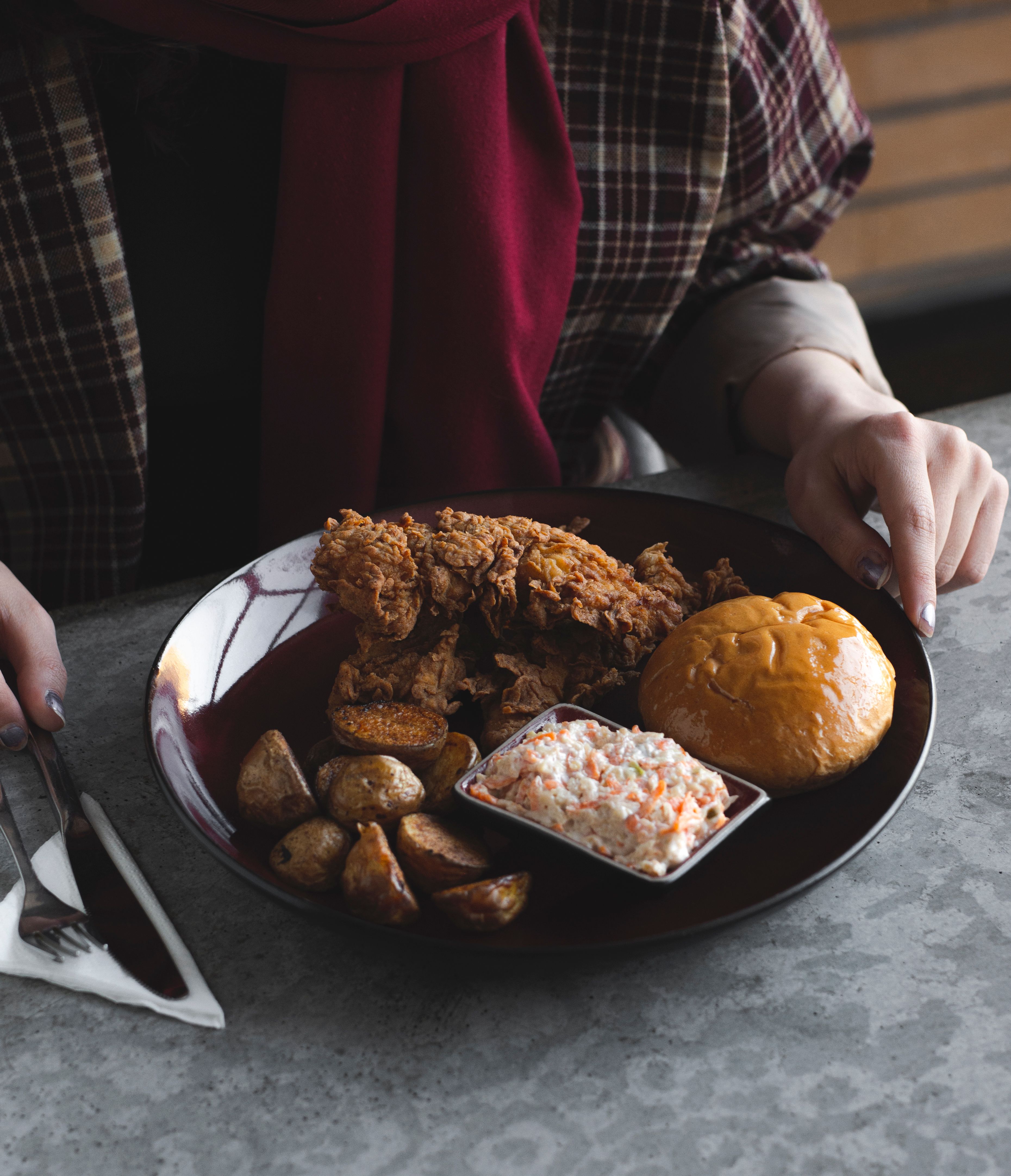 A delicious meal featuring crispy fried chicken, roasted potatoes, bread roll, and coleslaw on a plate.