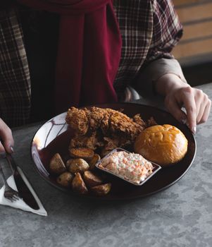 A delicious meal featuring crispy fried chicken, roasted potatoes, bread roll, and coleslaw on a plate.