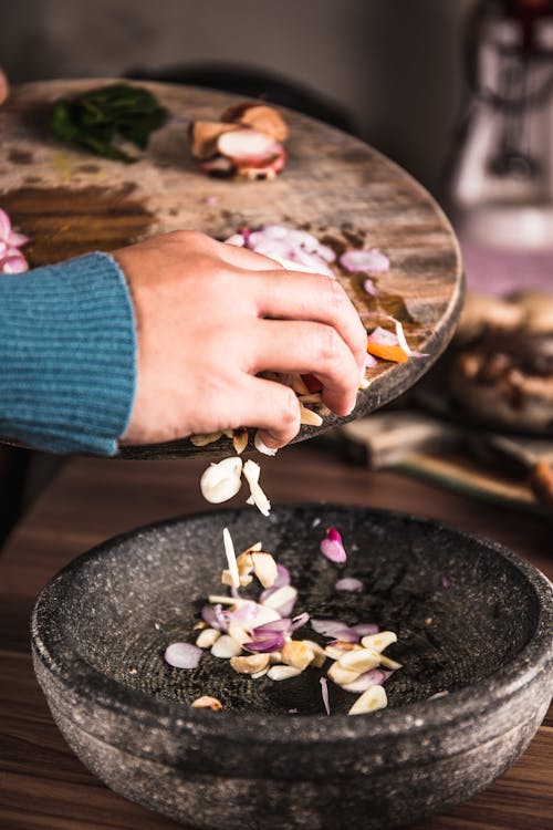 Person Pouring Sliced Spices from a Chopping Board to Black Bowl