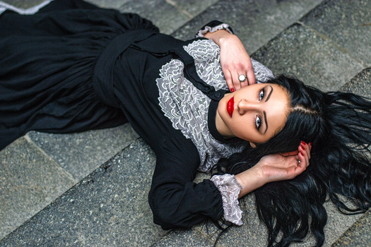 A stylish woman in a black lace dress lying elegantly on outdoor steps.