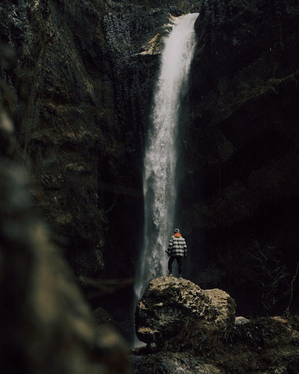 A Person Standing on a Rock Formation near Waterfalls