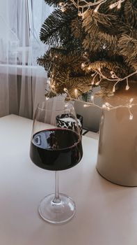 A glass of red wine next to a Christmas tree with lights, creating a festive holiday ambiance.