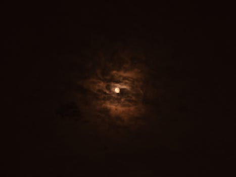 A moody night sky featuring the moon surrounded by dramatic clouds.