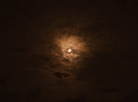 A dramatic full moon surrounded by dark, moody clouds in the night sky.