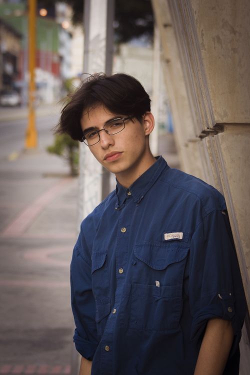 Free A young adult with eyeglasses poses casually outdoors in an urban setting wearing a blue shirt. Stock Photo