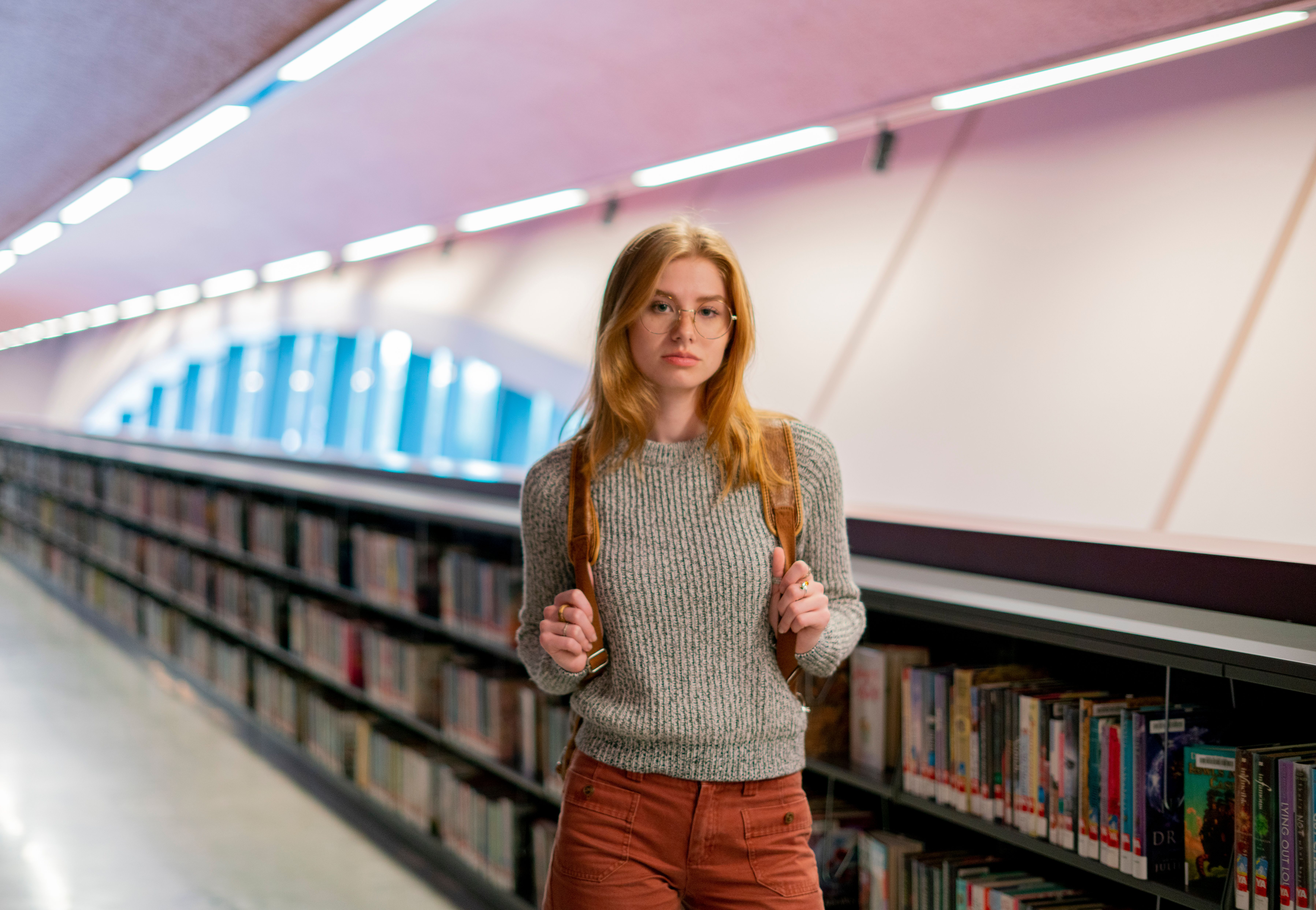 Portrait of a young woman with glasses in a modern library setting, focused on learning.