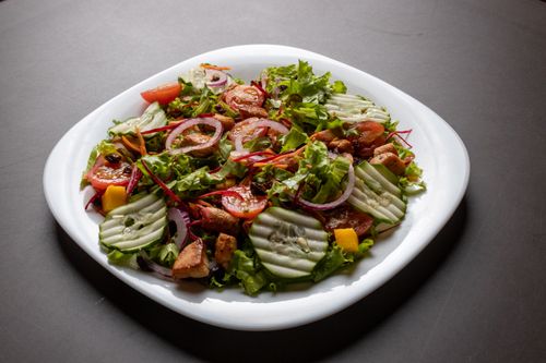 Free Delicious mixed vegetable salad featuring cucumbers, tomatoes, and greens on a white plate. Stock Photo