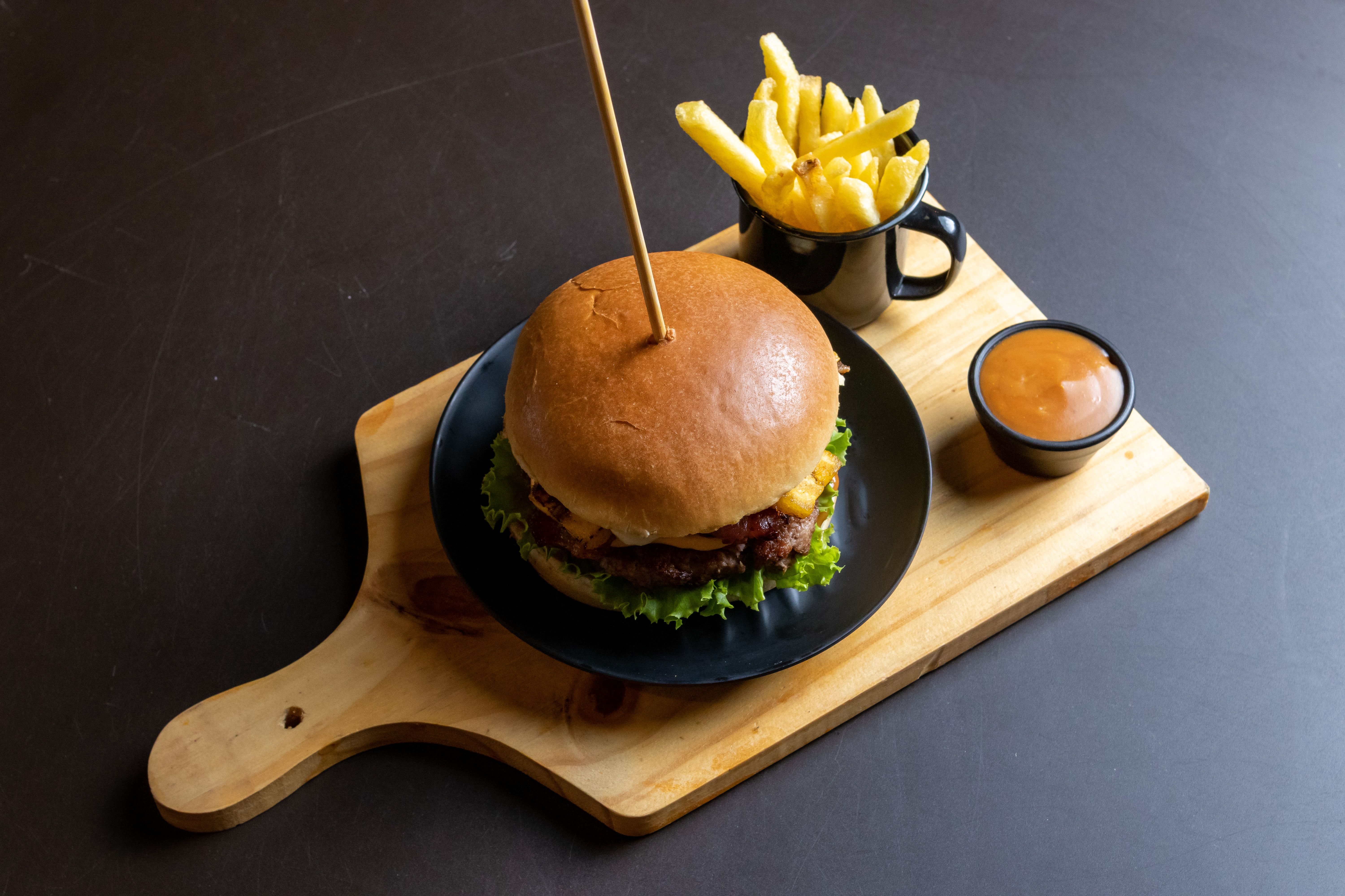 A delicious cheeseburger served with fries and dipping sauce on a wooden board.