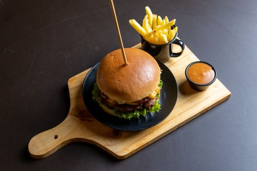 A delicious cheeseburger served with fries and dipping sauce on a wooden board.