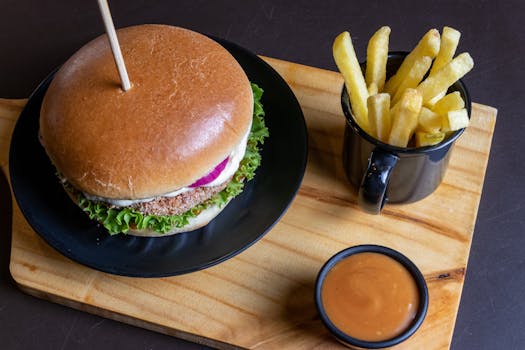 Top view of a tasty burger with fries and sauce on a wooden board.