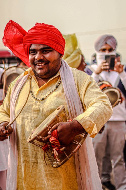 Free Cheerful performer in a red turban playing drums during a colorful cultural parade. Stock Photo