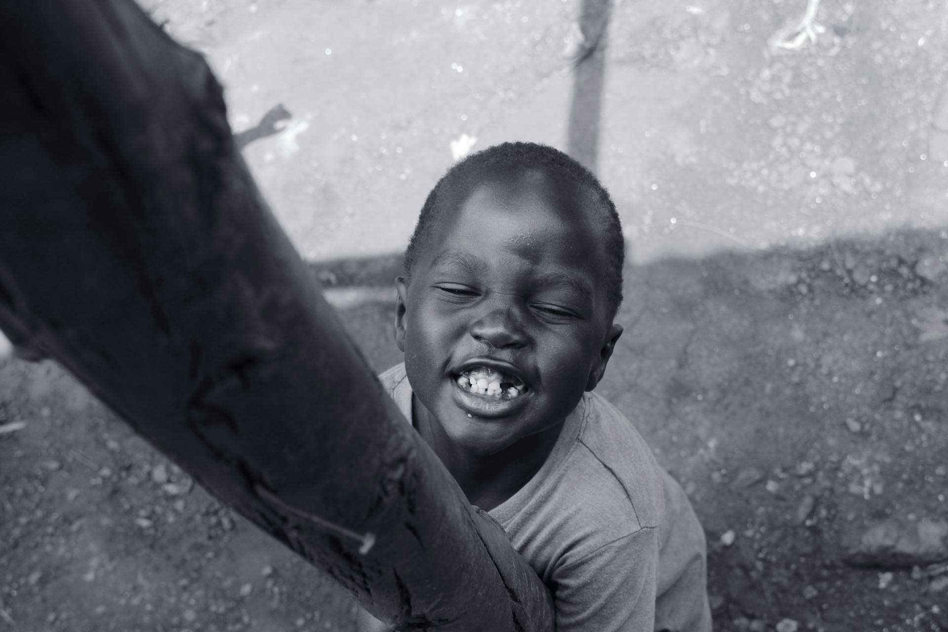 Black and white photo of a joyful child smiling outdoors in Kampala, Uganda