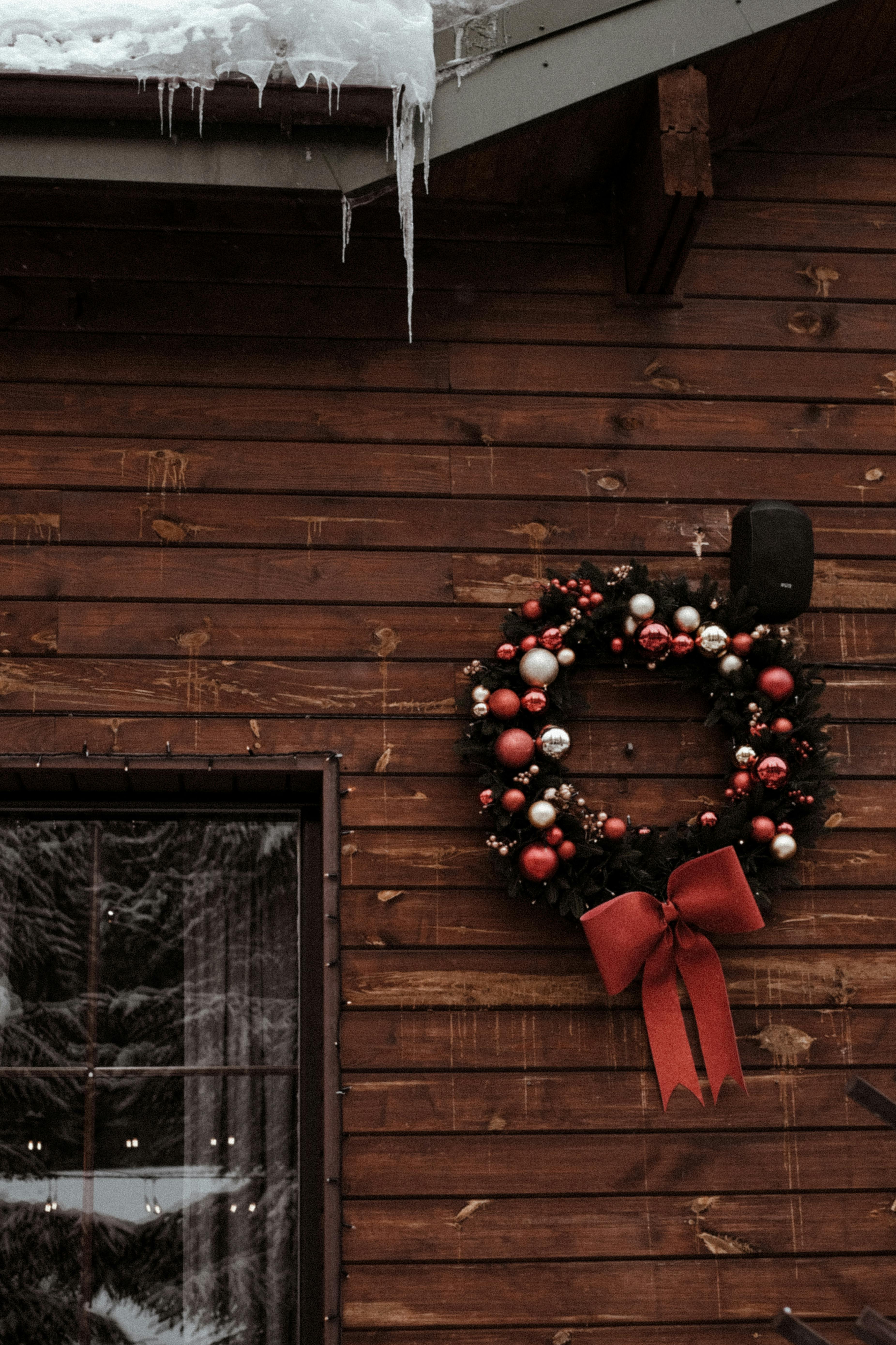 A decorative Christmas wreath with red and silver ornaments on a wooden wall with snow in Bukovel, Ukraine.