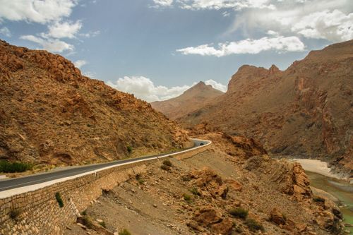 Free A winding road through rocky desert canyons with dramatic mountainous backdrop under cloudy skies. Stock Photo