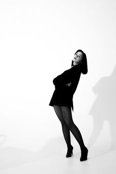 Elegant woman posing in black long-sleeved dress casting a shadow on a white background.