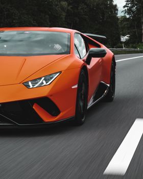 Vibrant orange Lamborghini Huracan speeding on an open highway, showcasing luxury and performance.