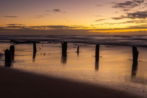 Free Tranquil sunset beach scene with weathered wooden posts and reflection in Brazil. Stock Photo