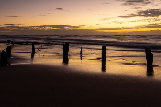 A serene sunset over wooden pier remnants on a Brazilian beach, offering a tranquil seascape view.