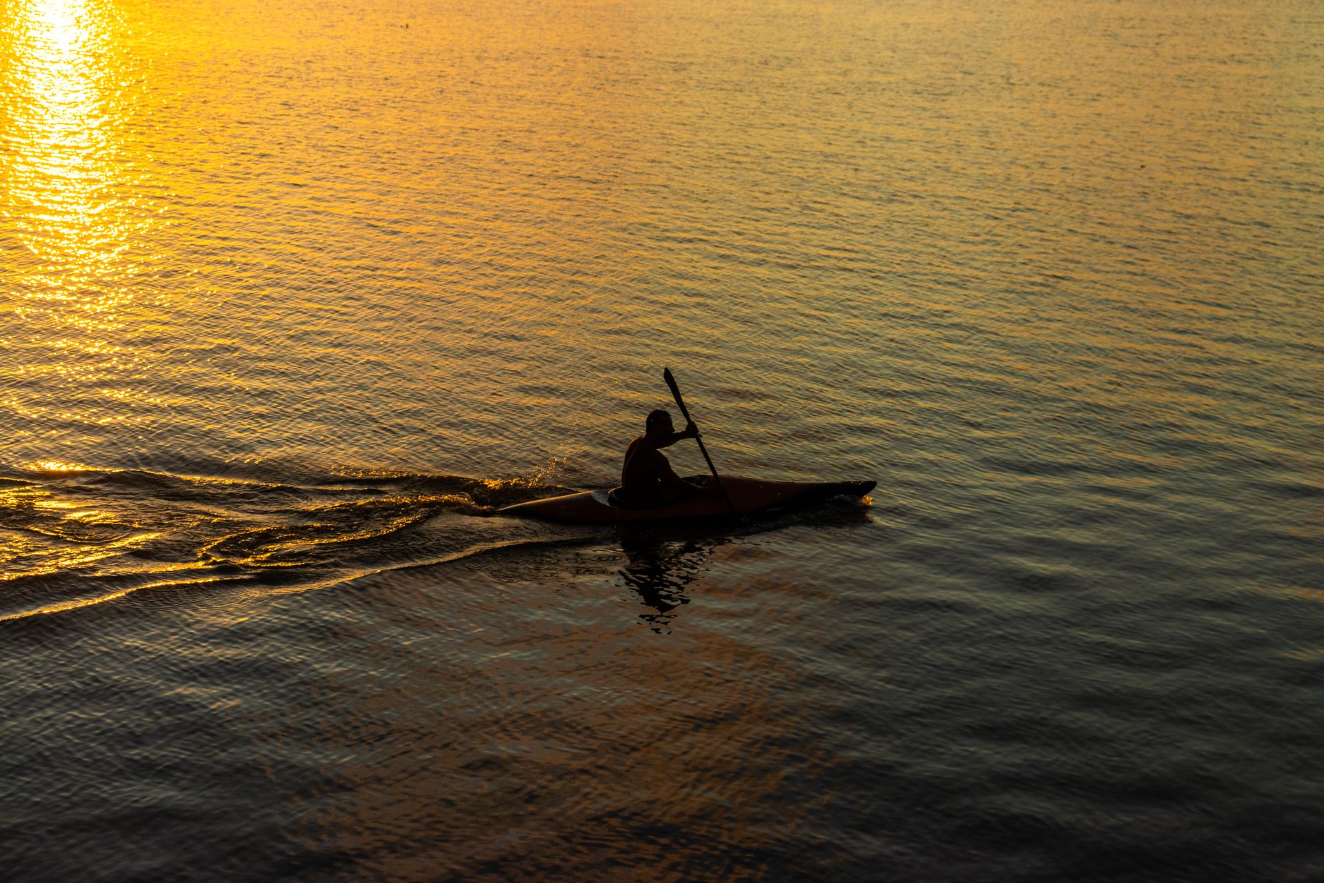 A kayaker paddling in silhouette against a stunning sunset on Brazilian waters, creating a tranquil