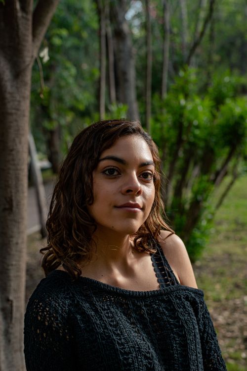 Free A young woman poses confidently outdoors, surrounded by greenery and trees. Stock Photo