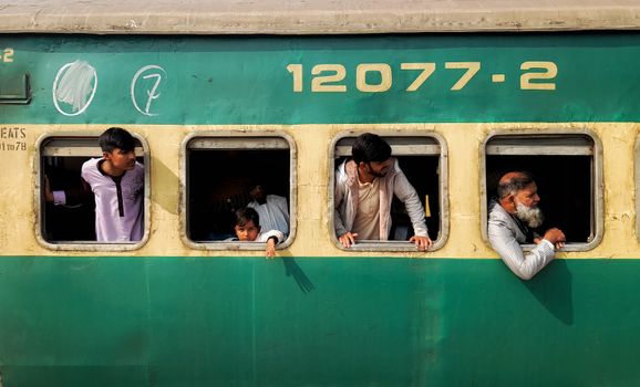 A group of passengers looking out from a moving train in Faisalabad, Punjab, reflecting daily commuting in Pakistan.